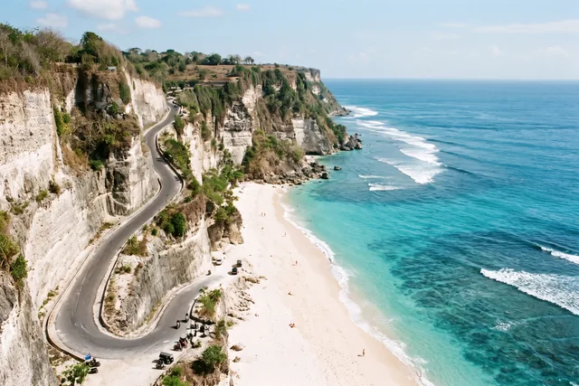 Biela pláž pod vápencovými útesmi a cesta vytesaná do skaly na juhu Bali