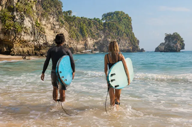 Dvaja surfisti s doskami vchádzajú do mora pod útesmi