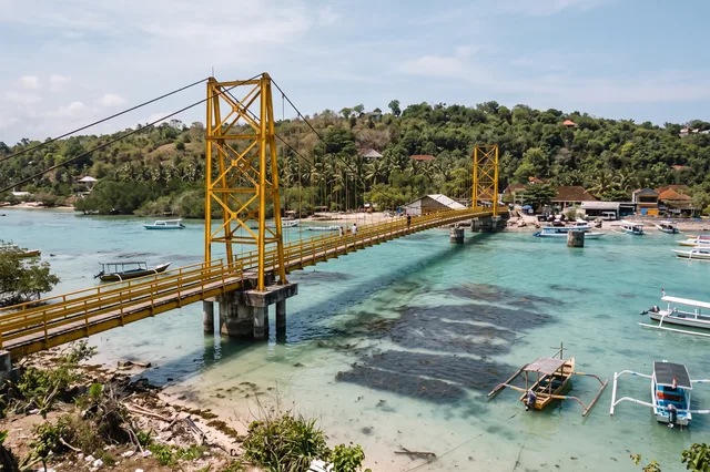 Žltý visutý most medzi Nusa Lembongan a Nusa Ceningan nad tyrkysovým kanálom s poliami morských rias