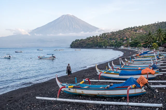 Colourful jukung fishing boats on the black-sand beach at Amed, Mount Agung behind the coast