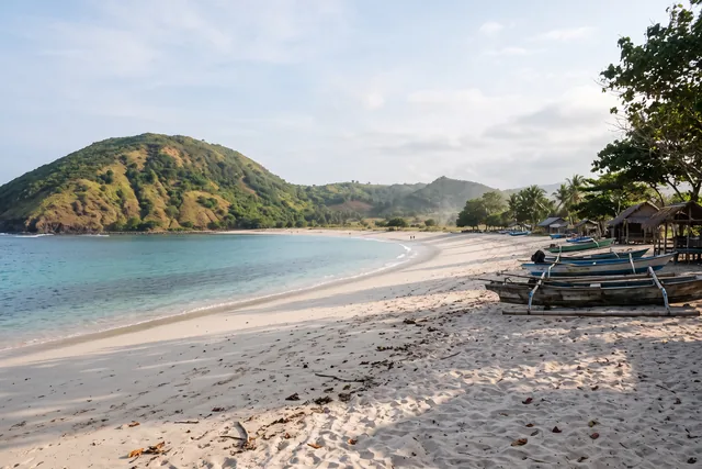 Mawun bay in south Lombok between green hills, with calm turquoise water and wooden boats on the sand
