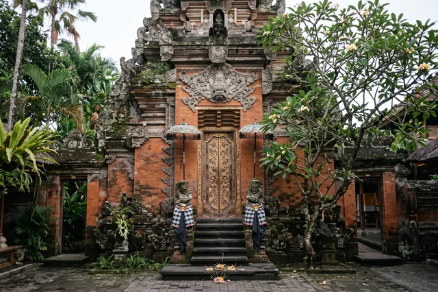 Carved gateway of Ubud Palace with offerings on the steps and guardian statues in black-and-white cloth