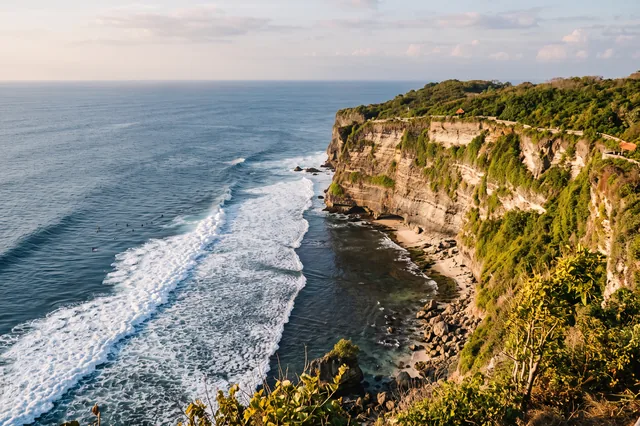Limestone cliffs at Uluwatu and waves breaking over the reef with a few distant surfers