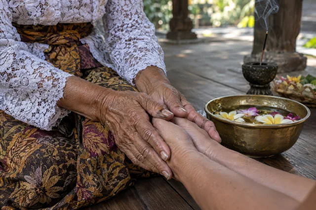 Illustrative image: an older woman's hands holding a visitor's hands beside a bowl of flowers
