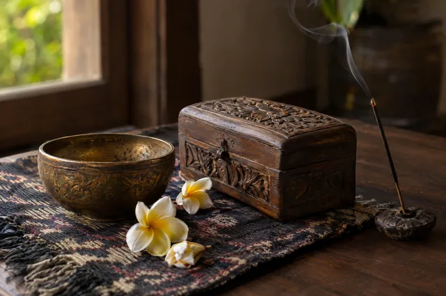 Illustrative image: a bronze bowl, a carved wooden box, flowers and incense