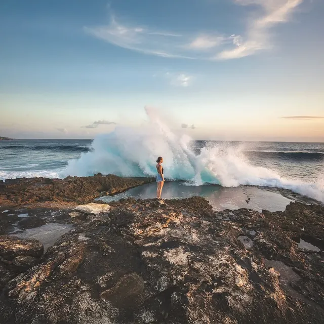 A wave breaking on the rocks, a woman standing on the cliff